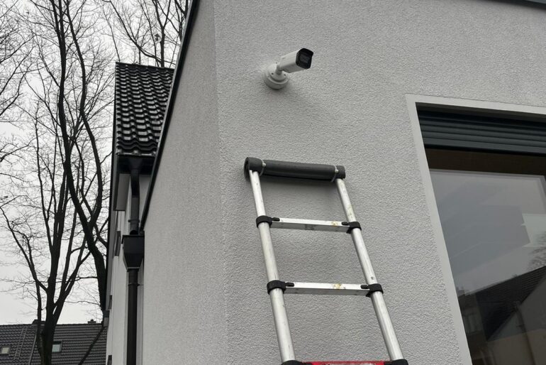 Montierte Außenkamera an einer Gebäudefassade mit Leiter im Vordergrund
